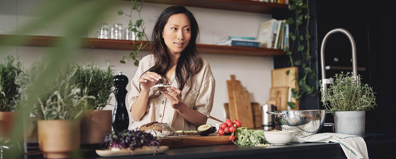 Vrouw staat in de keuken te genieten van een gezonde maaltijd. 